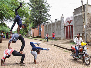 Girl performers from Arba Minch Circus build a human pyramid on the street while a confused motorbike rider passes by, Ethiopia, photo by Ivan Kralj