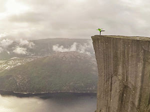 Man standing on one foot on the edge of Preikestolen or Pulpit Rock, square-shaped mountain plateau and the famous hiking destination at Lysefjord, Norway, photo by Ivan Kralj