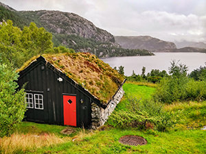 Black-walled house with red door and grass-covered roof at the shore of Revsvatnet lake, the starting point of Preikestolen / Pulpit Rock hike in Norway, photo by Ivan Kralj