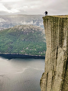 Man using a selfie stick to take photographs beyond the edge of Preikestolen or Pulpit Rock, square-shaped mountain plateau and the famous hiking destination at Lysefjord, Norway, photo by Ivan Kralj