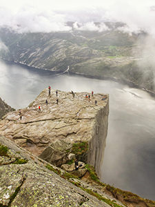 Preikestolen or Pulpit Rock, square-shaped mountain plateau and the famous hiking destination at Lysefjord, Norway, photographed from above, with people observing the surrounding from its edge, and clouds forming above the fjord, photo by Ivan Kralj