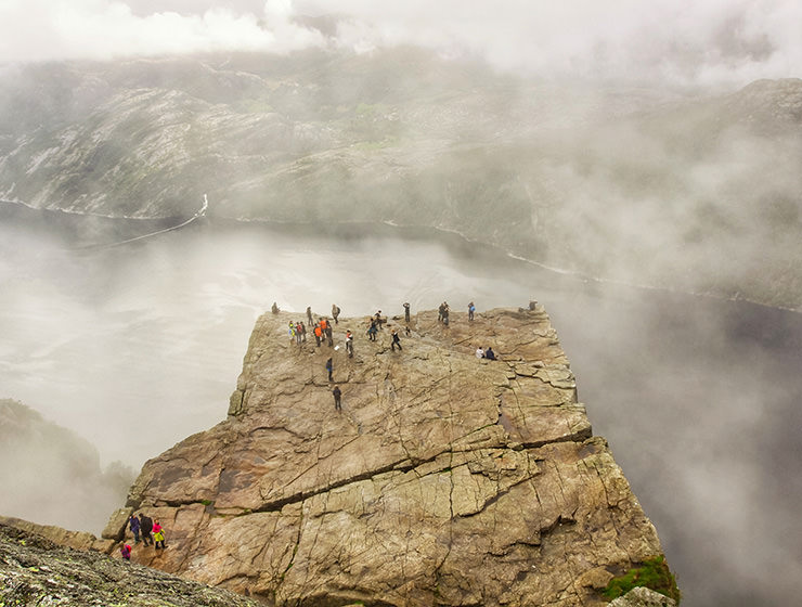 Preikestolen or Pulpit Rock, square-shaped mountain plateau and the famous hiking destination at Lysefjord, Norway, photographed from above, with people observing the surrounding from its edge, and clouds forming above the fjord, photo by Ivan Kralj