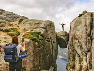 Girl photographing her friend standing on Kjeragbolten, a famous boulder on Kjerag Mountain, Norway, photo by Ivan Kralj