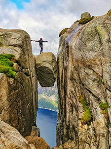 A girl using someone's assisting hand to step on Kjeragbolten, a famous boulder on Kjerag Mountain, Norway, photo by Ivan Kralj