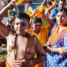 Young boy devotee with pierced tongue, carrying a paal kudam with his family at Thaipusam Festival 2019 at Batu Caves, Malaysia, photo by Ivan Kralj