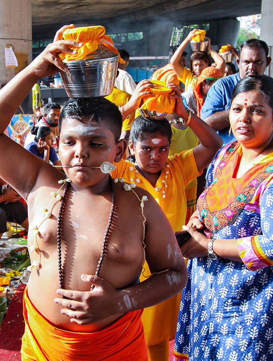Young boy devotee with pierced tongue, carrying a paal kudam with his family at Thaipusam Festival 2019 at Batu Caves, Malaysia, photo by Ivan Kralj