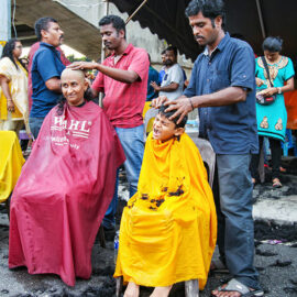 Woman and young boy getting their head shaved in the street at Thaipusam Festival 2019 at Batu Caves, Malaysia, photo by Ivan Kralj
