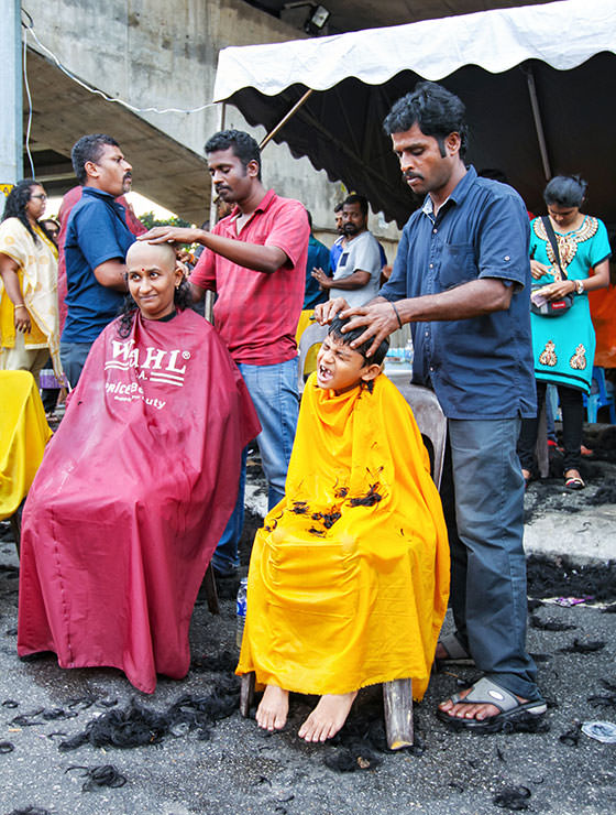 Woman and young boy getting their head shaved in the street at Thaipusam Festival 2019 at Batu Caves, Malaysia, photo by Ivan Kralj