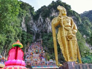 Gold statue of Lord Murugan next to the 272 stairs leading to Batu Caves, Malaysia. Pilgrims climbing them during the Thaipusam Festival 2019, photo by Ivan Kralj