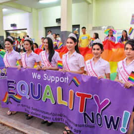 Crowned ladyboys holding the placard saying "we support equality now" in front of the huge rainbow flag at Chiang Mai Pride, gay parade in Chiang Mai, Thailand, photo by Ivan Kralj