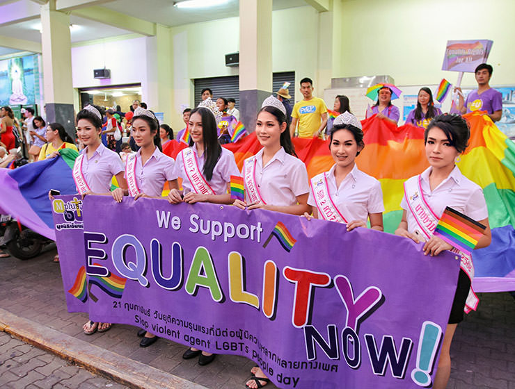 Crowned ladyboys holding the placard saying "we support equality now" in front of the huge rainbow flag at Chiang Mai Pride, gay parade in Chiang Mai, Thailand, photo by Ivan Kralj