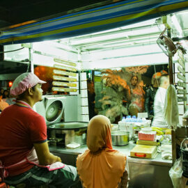 Participant with feathers at Chiang Mai Pride, gay parade in Chiang Mai, Thailand, passing by traditionally dressed roti makers' food station, photo by Ivan Kralj