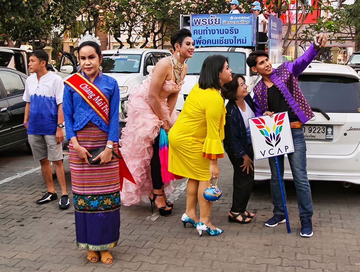 Crowned participant standing while some other participants are taking a selfie in the background at Chiang Mai Pride, gay parade in Chiang Mai, Thailand, photo by Ivan Kralj