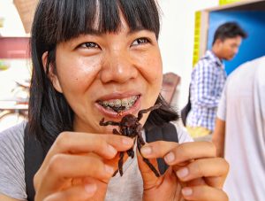 Kim Peou, with braces on her teeth, eating a scorpion at Backstreet Academy's Fear Factor Challenge, in Siem Reap, Cambodia, country where they love to eat insects, photo by Ivan Kralj