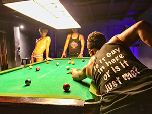 Young men playing pool at the Toolbox bar in Phnom Penh, Cambodia, the player is wearing a T-shirt saying "Is it Gay in here or is it just me?", photo by Ivan Kralj
