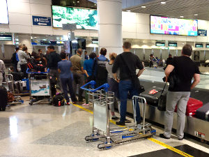 Airport passengers crowding behind the yellow line of the baggage carousel, photo by Ivan Kralj
