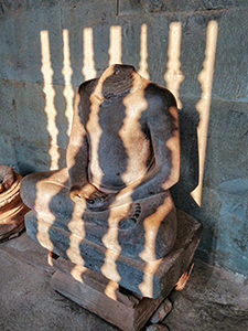 Headless Buddha statue with a shadow of stone windows at Angkor Wat during sunset, in Cambodia, photo by Ivan Kralj