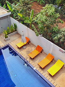 Blue swimming pool with orange and yellow sun loungers and tropical vegetation behind, at Sleep Pod Hostel in Siem Reap, Cambodia, photo by Ivan Kralj