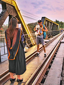 A man posing for a cheerful photo with two dogs in a frontpack, on the Bridge on the River Kwai, a part of the Death Railway in Kanchanaburi, Thailand, photo by Ivan Kralj