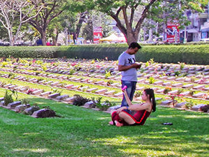 A woman checking how did her selfie in the grass at Kanchanaburi War Cemetery turn out, Kanchanaburi, Thailand, photo by Ivan Kralj