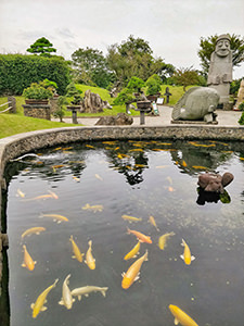Pond with koi fish at bonsai park Spirited Garden, with the sculpture of dol hareubang, the local grandfather deity, Jeju Island, South Korea, photo by Ivan Kralj