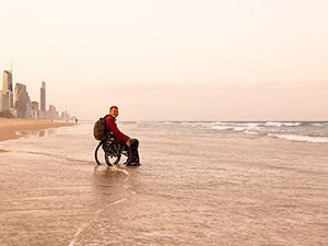 Traveler Slaven Škrobot sitting in a wheelchair on a beach in Australia with the waves covering the area with water