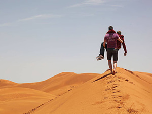A friend is carrying Slaven Škrobot, a disabled traveler, on a dune in Sahara, Morocco