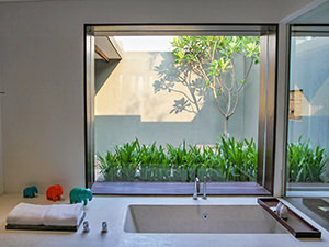 Bathtub in the courtyard suite of The Balé Phnom Penh resort, with a private green patio behind the large window glass, Cambodia, photo by Ivan Kralj