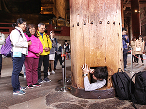 A young man squeezing through the hole in the pillar at Todai-ji temple, those who can pass through will achieve enlightenment in their next life, according to this Shinto belief, Nara, Japan, photo by Ivan Kralj
