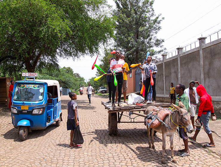 Performers from Arba Minch Circus juggling colorful clubs on a carriage pulled by a donkey through the street of their town, while passers-by and tuk-tuk driver observe, Ethiopia, photo by Ivan Kralj