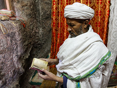 Priest in Bet Meskel, a tiny Lalibela church, with proportionally small Bible in his hands. Lalibela, Ethiopia. Photo by Ivan Kralj