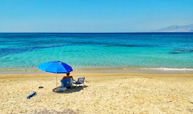 Man sitting alone under a parasol on a sandy beach in Naxos, Greece, in the times of social distancing due to coronavirus epidemic, photo by Ivan Kralj