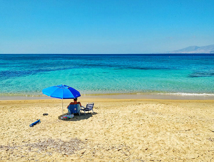 Man sitting alone under a parasol on a sandy beach in Naxos, Greece, in the times of social distancing due to coronavirus epidemic, photo by Ivan Kralj