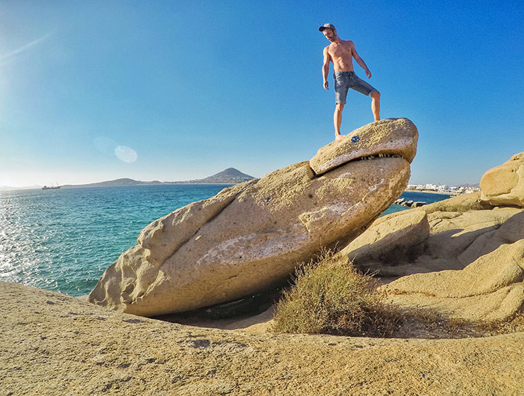 Travel blogger Ivan Kralj standing on a shark-shaped rock on Agia Anna Beach, one of the more unusual things to do in Naxos, Greece, photo by Ivan Kralj
