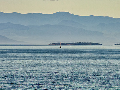 Bert terHart's sailboat as a tiny dot on the sea with islands and mountains in the back