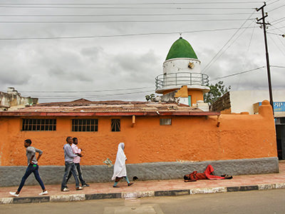 People passing by a mosque and a man lying in the street in Harar, Ethiopia, photo by Ivan Kralj