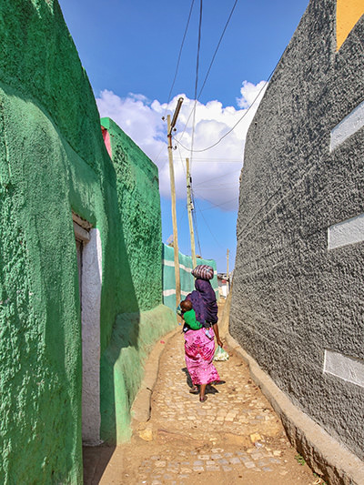 Harar woman in colorful clothing passing through the narrow alley of Jugol, the old city of Harar, with colorful walls of compounds, Ethiopia, photo by Ivan Kralj
