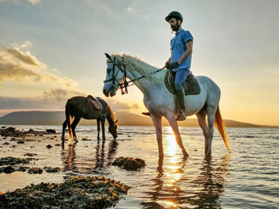Ivan Kralj riding a white Australian horse in the shallow waters of Sentigi Beach in West Bali National Park, Indonesia, at sunset