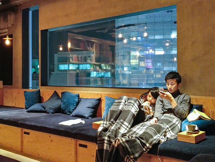 A couple spending their Valentine's Day 'at home', under a blanket, looking at mobile phones, shot at Book and Bed Hostel in Tokyio, Japan, photo by Ivan Kralj