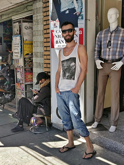 Pipeaway blogger Ivan Kralj dressed in sleeveless shirt, capri pants, flip-flops and sunglasses, standing next to the shopseller woman crouching in winter clothes, in Dalat, the City of Eternal Spring, in Vietnam