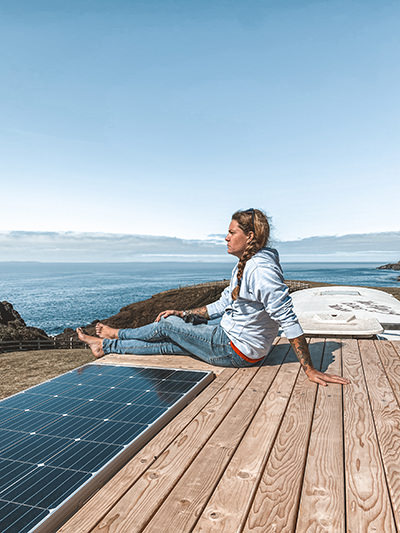 Jessica Rambo enjoying the views of nature while sitting on the top of her converted school bus / house on wheels next to the solar panels, Painted Buffalo Traveling Studio