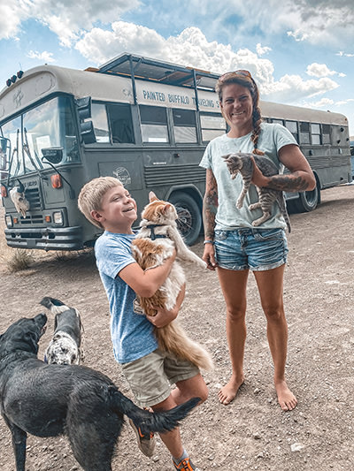 Jessica Rambo, American Marine Corps veteran and artist, standing in front of her converted skoolie Painted Buffalo Traveling Studio, with her son Liam, dogs and cats