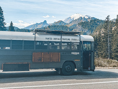 Painted Buffalo Traveling Studio, a converted school bus with mountains as a backdrop