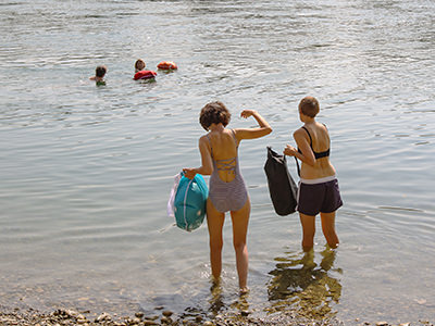 Two women with Wickelfisch waterproof bags entering the Rhine, a popular place for swimming during the summer. Rheinschwimmen is one of the most fun things to do in Basel. Photo by Ivan Kralj