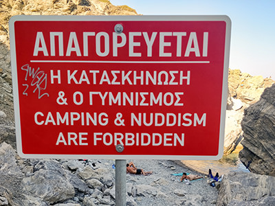 Nudists sunbathing behind the nudism-forbidding sign at Agia Anna Beach in Amorgos, Cyclades, Greece, photo by Ivan Kralj