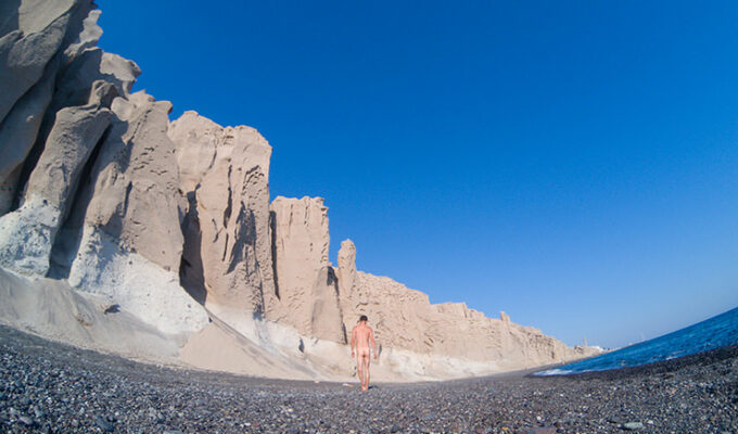 Naked man walking on the black sand and under the bright cliffs of Vlichada Beach in Santorini, one of the best nude beaches in Cyclades Islands, Greece, photo by Ivan Kralj