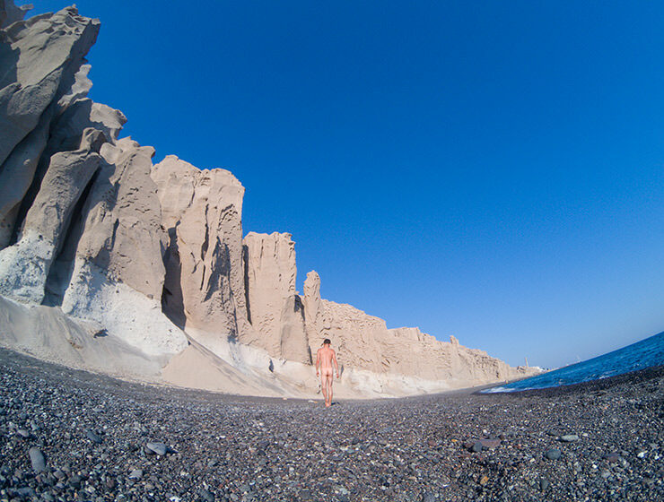 Naked man walking on the black sand and under the bright cliffs of Vlichada Beach in Santorini, one of the best nude beaches in Cyclades Islands, Greece, photo by Ivan Kralj