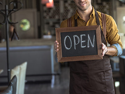 Waiter holding board with 'Open' chalk inscription in cafe, photo by AllaSerebrina, Depositphotos