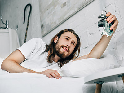 Bearded man turning off the alarm clock while in bed, photo by Vitalik Radko / Depositphotos.com