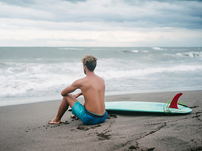 Surfer with surfing board, sitting on a sandy beach in Bali, Indonesia, one of the destinations rising in popularity in travel trends 2022, photo by YuliyaKirayonakBO / Depositphotos.com